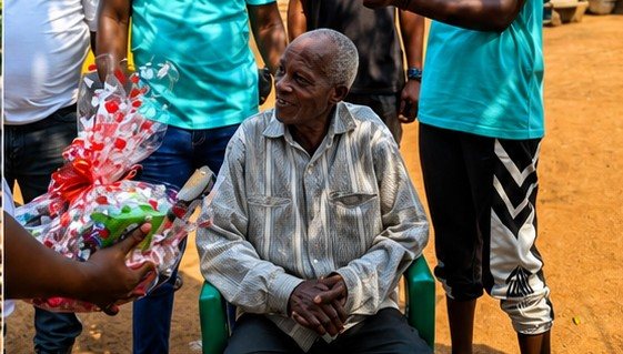 A volunteer presenting a gift to a seated elderly man